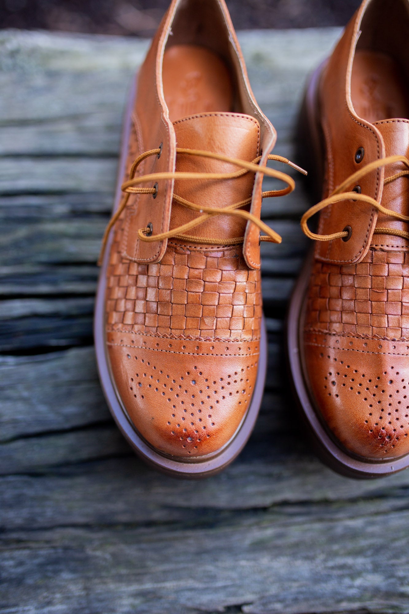 Pair of brown leather shoes with woven pattern on a wooden surface
