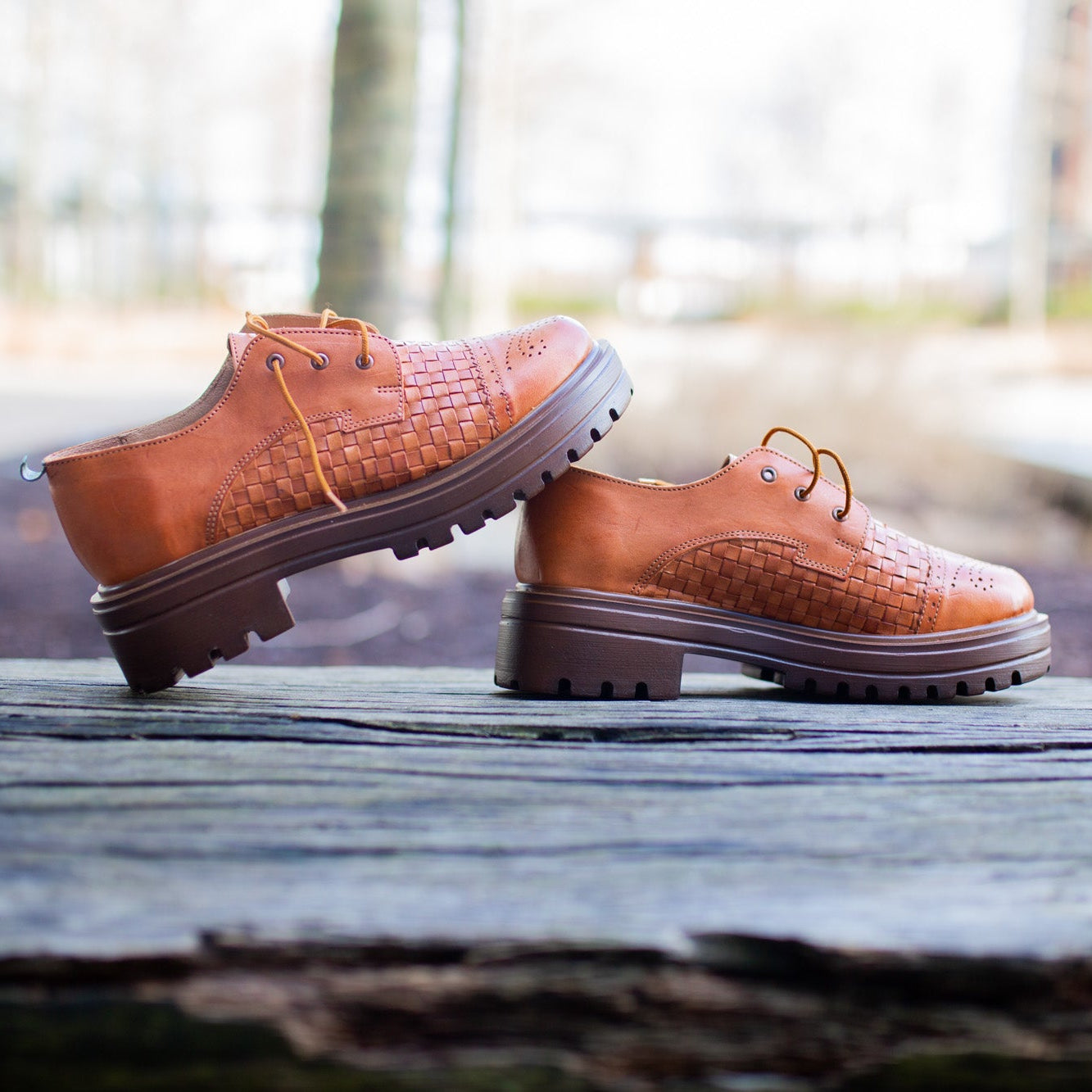 Pair of brown leather shoes on a wooden surface with a blurred natural background