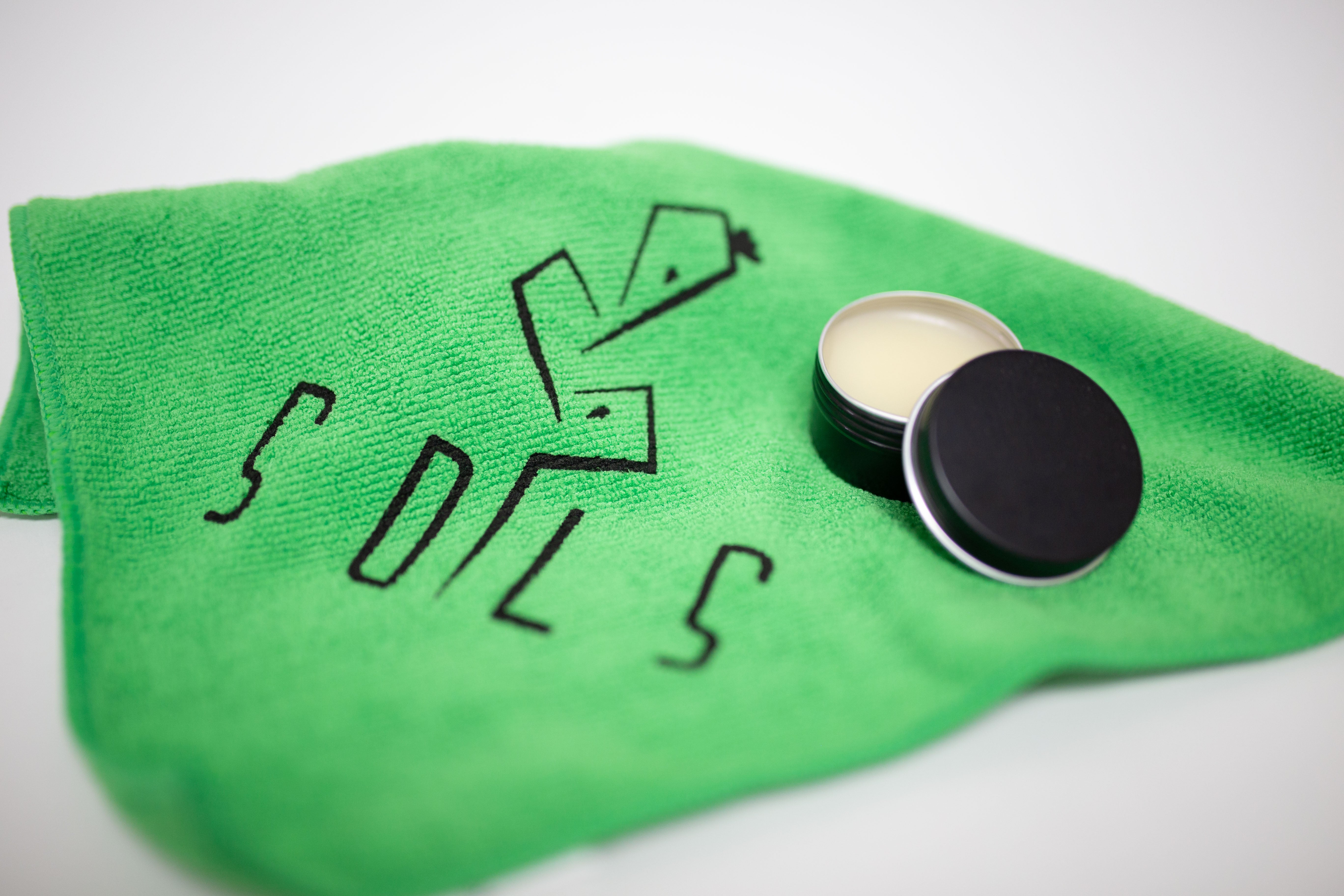 black metal container with leather conditioner inside, on top of green towel with SOLS cactus logo